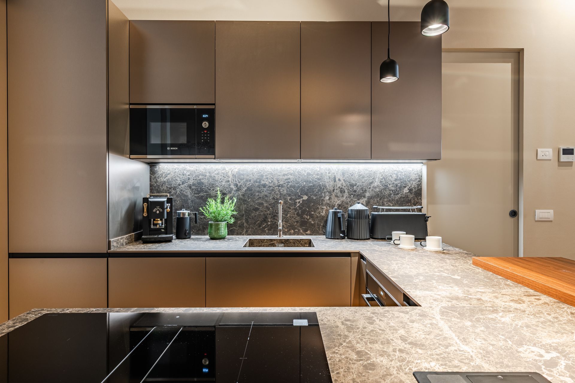 Front view of the kitchen with taupe cabinets, backlit marble backsplash and Molinari machine