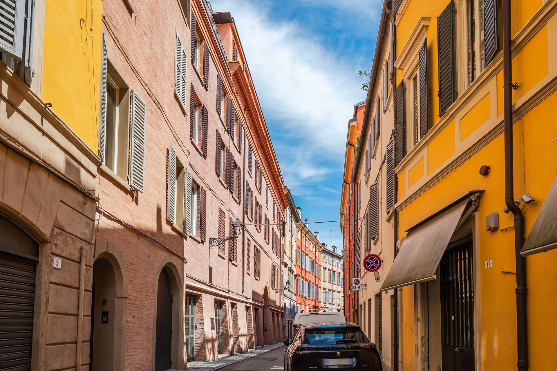 Via del centro storico di Modena con facciate gialle, rosa e cielo azzurro