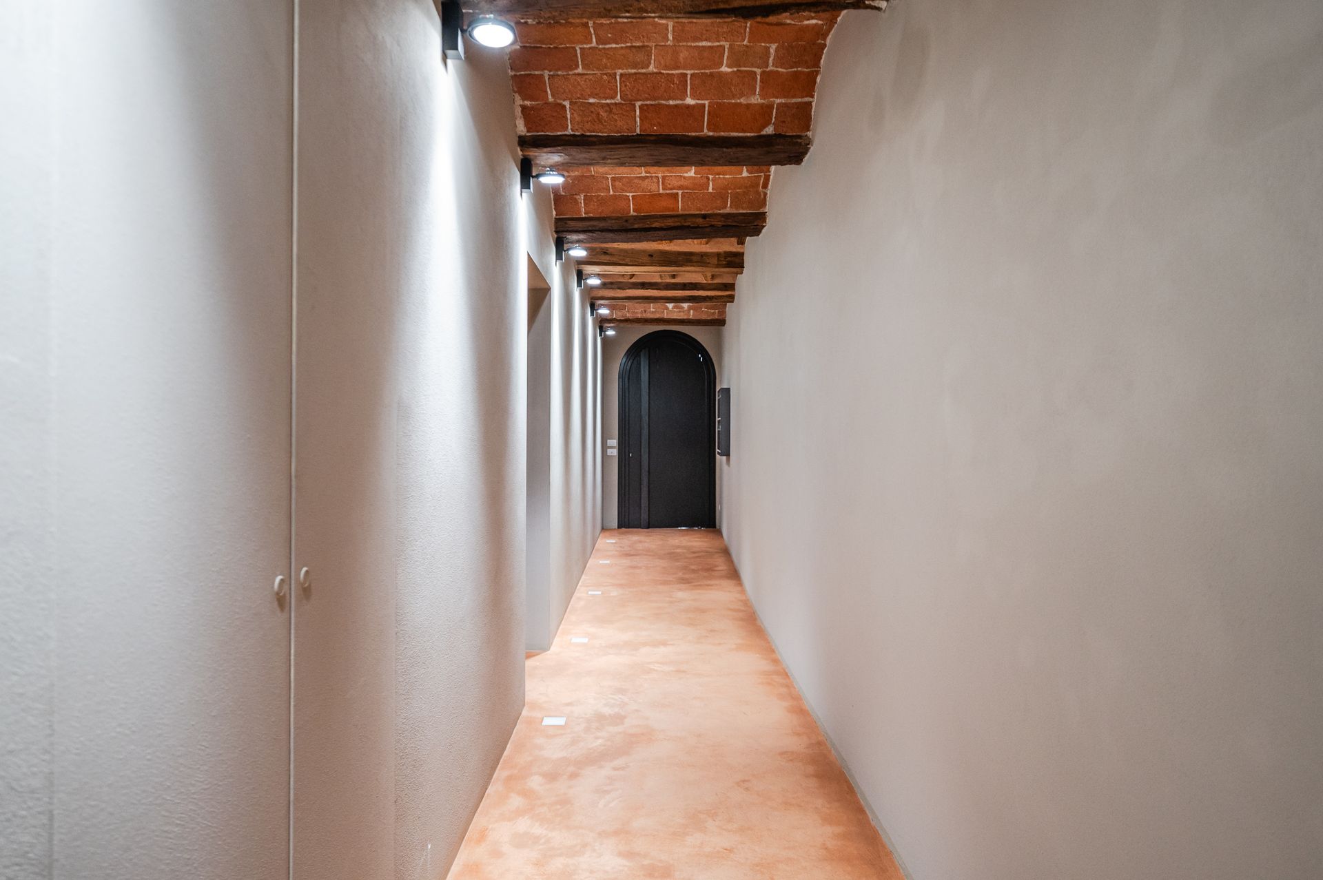 Corridor with exposed brick vaults and an arched door at the far end